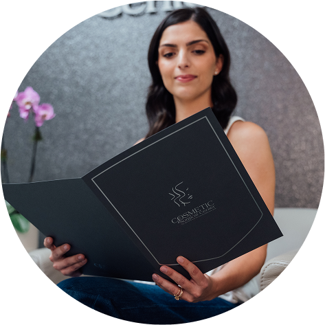 A circular close-up of a patient holding a black informational folder. The folder features the "Cosmetic Surgical Center" logo in silver.